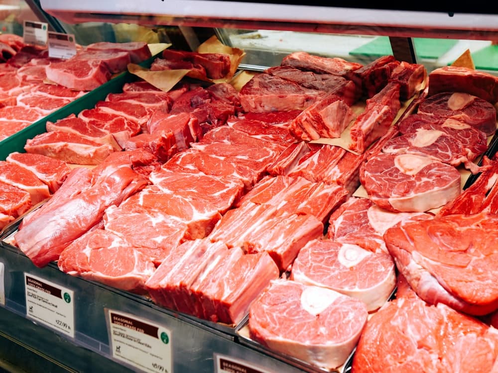 A butcher's chilled display counter filled with cuts of meat and price labels.